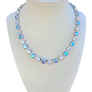 Puede incluir: Un collar brillante con cristales redondos e iridiscentes en tonos azules y blancos. Los cristales están engarzados en un metal plateado, creando una joya glamurosa. El collar se exhibe en un maniquí.