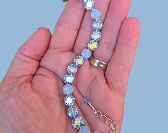 May include: A silver-toned bracelet featuring a series of round, iridescent, light-reflecting crystals. The bracelet includes a metal chain extension with a small dangling crystal charm at the end, showcasing a multi-colored shimmer.
