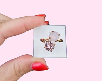 May include: A gold ring with two clear stones. The larger stone is a pale pink and the smaller stone is white.