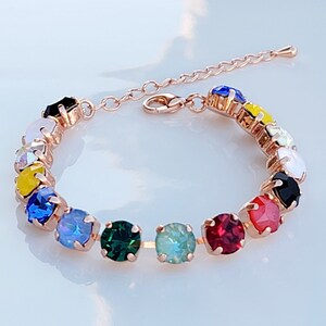 May include: A rose gold bracelet with a chain and a row of colorful crystal stones. The stones are in a rainbow pattern, with red, orange, yellow, green, blue, indigo, and violet.