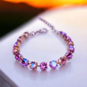 Op de afbeelding: Een delicate armband met een zilveren ketting en iriserende roze en paarse kristallen.