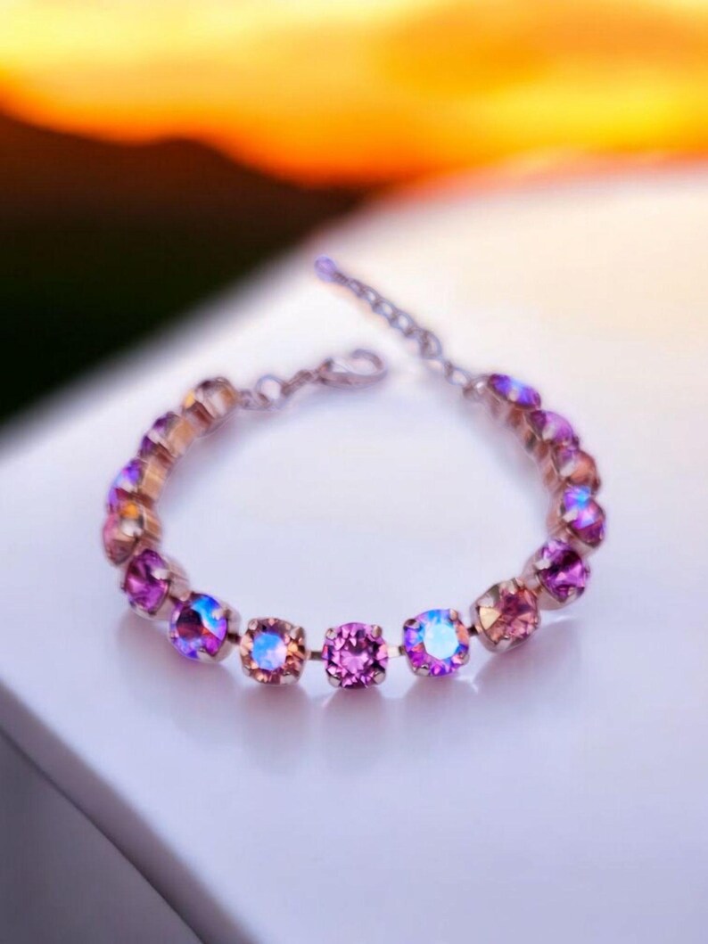 Op de afbeelding: Een delicate armband met een zilveren ketting en iriserende roze en paarse kristallen.