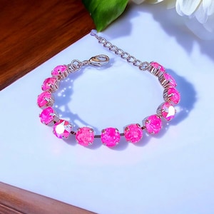 May include: A silver bracelet with a chain link design and pink crystal stones. The bracelet is made of metal and has a clasp closure.