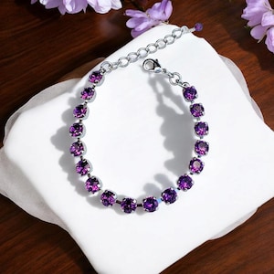 May include: A silver chain bracelet with a lobster clasp closure. The bracelet is adorned with a row of round, purple crystals.