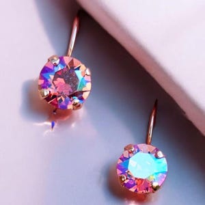 May include: A pair of rose gold earrings with iridescent pink and blue gemstones. The earrings have a simple, elegant design.