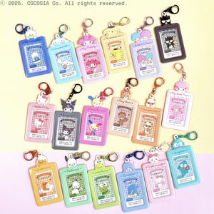 May include: Collection of character ID badge holders with keychains. Each holder features a different cartoon character, including Hello Kitty, My Melody, and others. The holders are rectangular with a clear window and colorful borders.