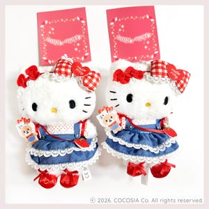 Puede incluir: Dos peluches de Hello Kitty blancos con vestidos de mezclilla azul, ribetes de encaje blanco, lazos de cuadros rojos y blancos y zapatos rojos. Cada peluche incluye un pequeño dije y una etiqueta roja con el texto Hello Kitty arriba.