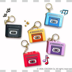 May include: A collection of colorful cassette tape keychains in black, blue, yellow, red, and purple. Each keychain features a miniature cassette tape design with a gold-colored keyring and chain. Musical notes are also included.