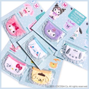 Op de afbeelding: Assortiment van baby slabbetjes met karakterthema's in verschillende kleuren, waaronder roze, paars, wit en geel. Elke slab heeft een ander cartoon karakterontwerp en is afgewerkt met kant. De slabbetjes zijn verpakt op blauwe kaarten met Japanse tekst.