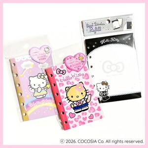 Könnte beinhalten: Drei Schreibwarenartikel zum Thema Hello Kitty. Zwei kleine Ringbücher zeigen Hello Kitty-Designs und den Text "Hello Kitty". Ein dritter Artikel ist eine Nachfüllpackung für einen Siegelordner. Die Artikel sind in durchsichtigem Kunststoff verpackt.