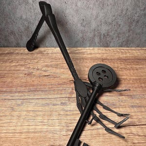 May include: Black decorative key with a round top and a detailed handle. The key is resting on a wooden surface. The key's design includes a circular top with four holes and a detailed handle.