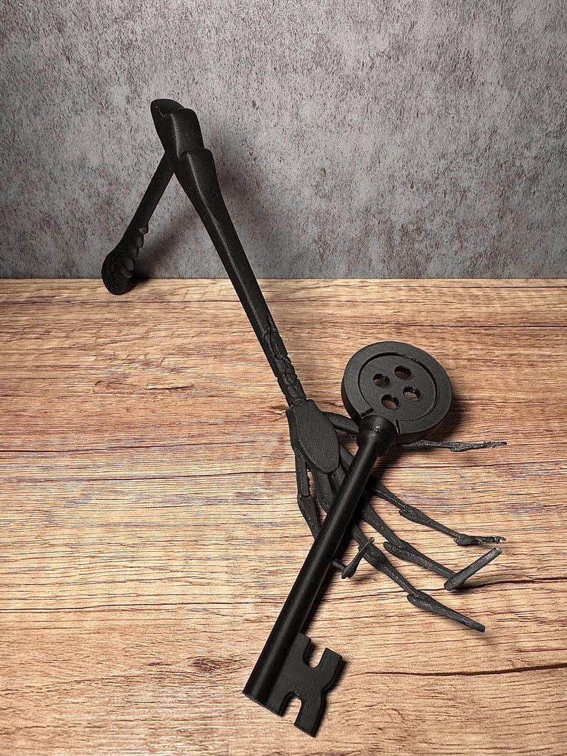 May include: Black decorative key with a round top and a detailed handle. The key is resting on a wooden surface. The key's design includes a circular top with four holes and a detailed handle.