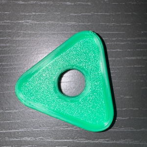 May include: A bright green, triangular object with a circular hole in the center. The edges are rounded, and the surface has a textured appearance. The object is likely a small, decorative item or a component of a larger product.