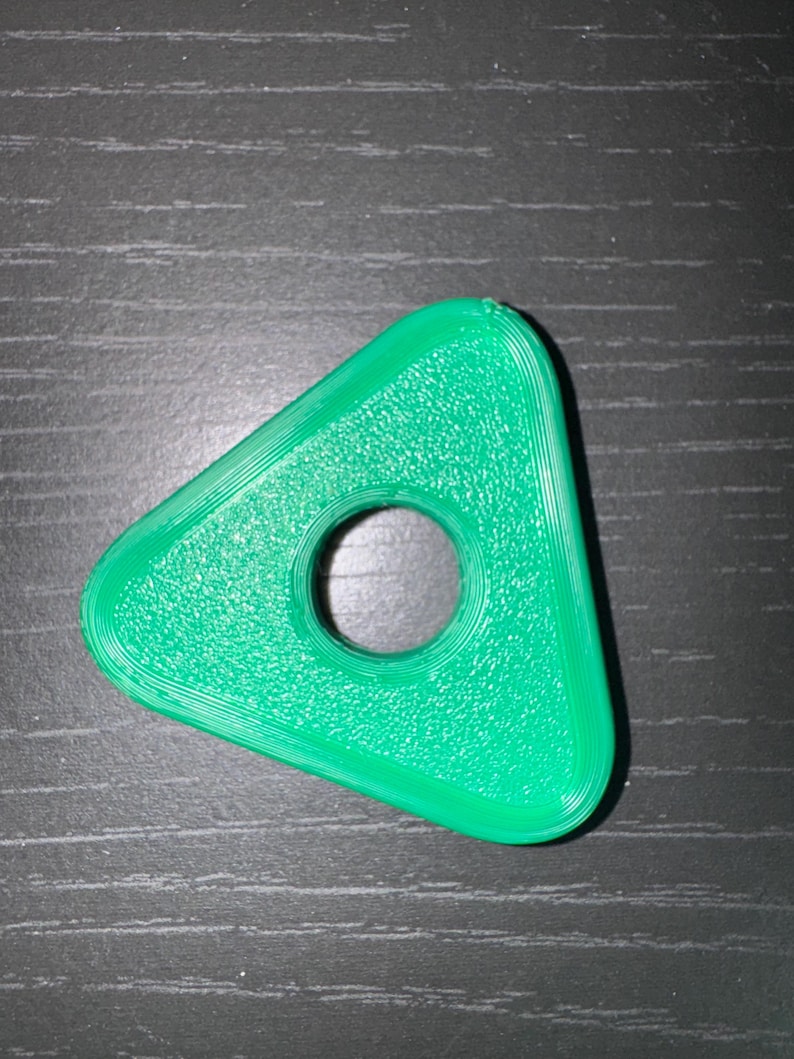 May include: A bright green, triangular object with a circular hole in the center. The edges are rounded, and the surface has a textured appearance. The object is likely a small, decorative item or a component of a larger product.