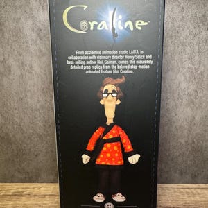 May include: A box featuring the Coraline movie logo and a doll of the Other Father character. The doll wears a red jacket with orange polka dots, black pants, and white shoes. The box includes text about the film and the doll's origin.