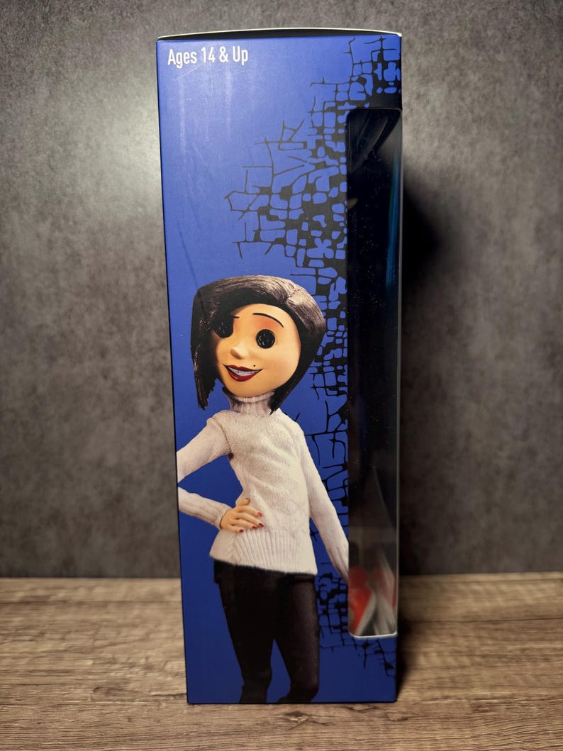 May include: Ages 14 & Up. Boxed doll featuring a character with black hair, a white turtleneck sweater, and black pants. The box has a blue background with a graphic design and a clear plastic window. The doll is a collectible item.