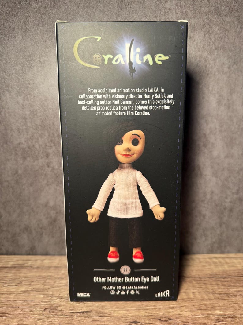 May include: A box featuring the Coraline movie doll, Other Mother Button Eye Doll. The doll is wearing a white sweater, black pants, and red shoes. The box has the Coraline logo and text from the movie.
