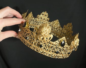 Peut inclure: Une couronne dorée ornée de pierres précieuses noires et d'une tête de lion. La couronne est faite d'un travail de métal complexe et présente un design délicat et orné.