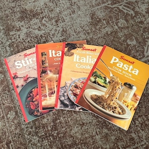May include: A collection of four Sunset brand cookbooks featuring titles Stir-Fry, Italian Cooking, and Pasta. Each softcover book displays vibrant food photography on the front cover, including images of cooked pasta, stir-fry, and cheese dishes.