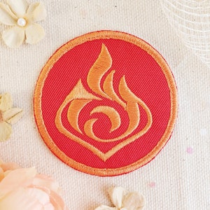 May include: A red embroidered patch with a gold flame design. The flame is stylized and has a swirling pattern.