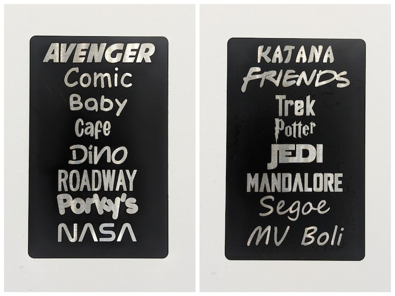 May include: Two black rectangular signs with silver lettering. The left sign has the words "AVENGER", "Comic", "Baby", "Cafe", "Dino", "ROADWAY", "Porky's", and "NASA". The right sign has the words "KATANA", "FRIENDS", "Trek", "Potter", "JEDI", "MANDALORE", "Segoe", "MV Boli".