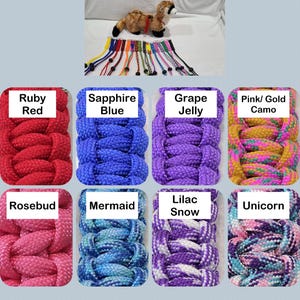 May include: A variety of colorful braided dog collars are displayed, each labeled with a unique color name. Colors include Ruby Red, Sapphire Blue, Grape Jelly, Pink/Gold Camo, Rosebud, Mermaid, Lilac Snow, and Unicorn. A stuffed animal is also present.