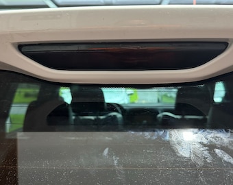 May include: A close-up of the rear window of a white car. The window is dirty and has a lot of dust and dirt on it. The rear window wiper is visible at the top of the window.