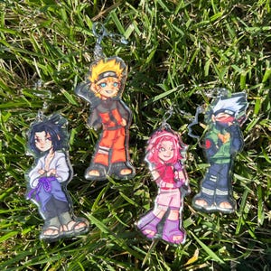 K&ouml;nnte beinhalten: Vier Acryl-Schl&uuml;sselanh&auml;nger mit Anime-Charakteren. Die Charaktere sind Naruto, Sasuke, Sakura und Kakashi. Jeder Schl&uuml;sselanh&auml;nger hat eine silberfarbene Kette und ein klares, gl&auml;nzendes Finish. Die Charaktere sind in leuchtenden Farben dargestellt.