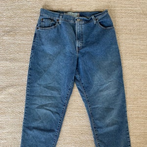 Puede incluir: Un par de pantalones vaqueros azules de mezclilla con corte recto. Los vaqueros tienen un estilo clásico de cinco bolsillos y cierre de botón.