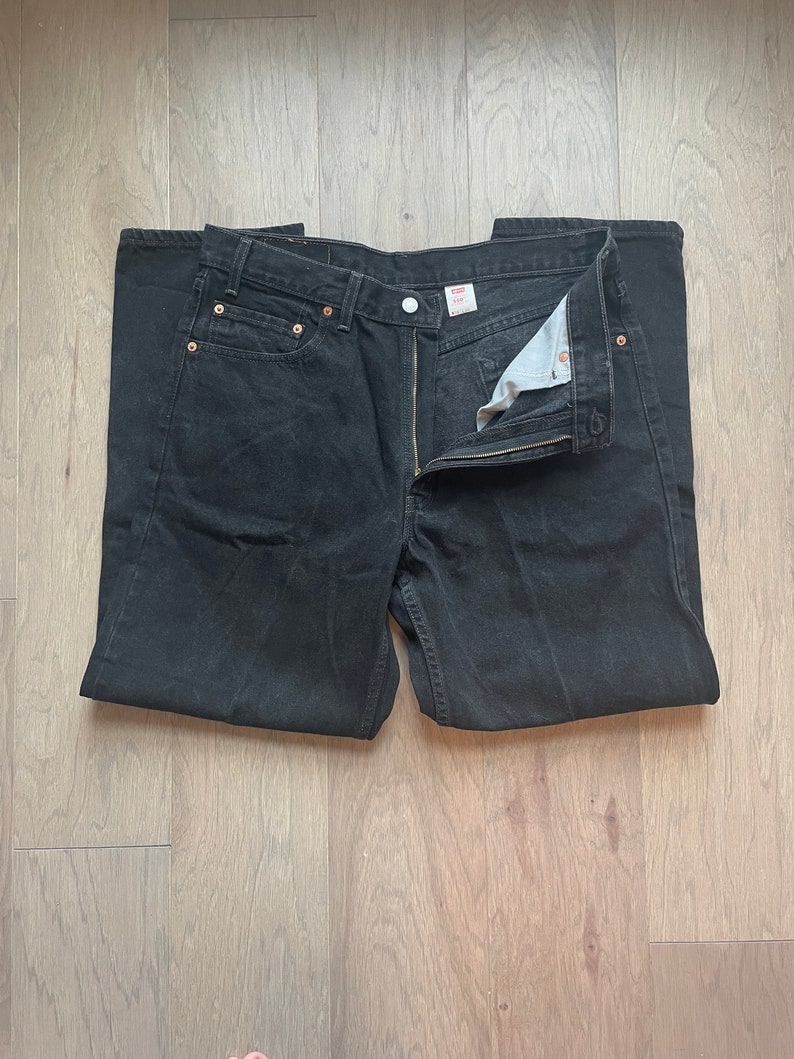 May include: A pair of black denim jeans with a button fly and a Levi's label on the back pocket.