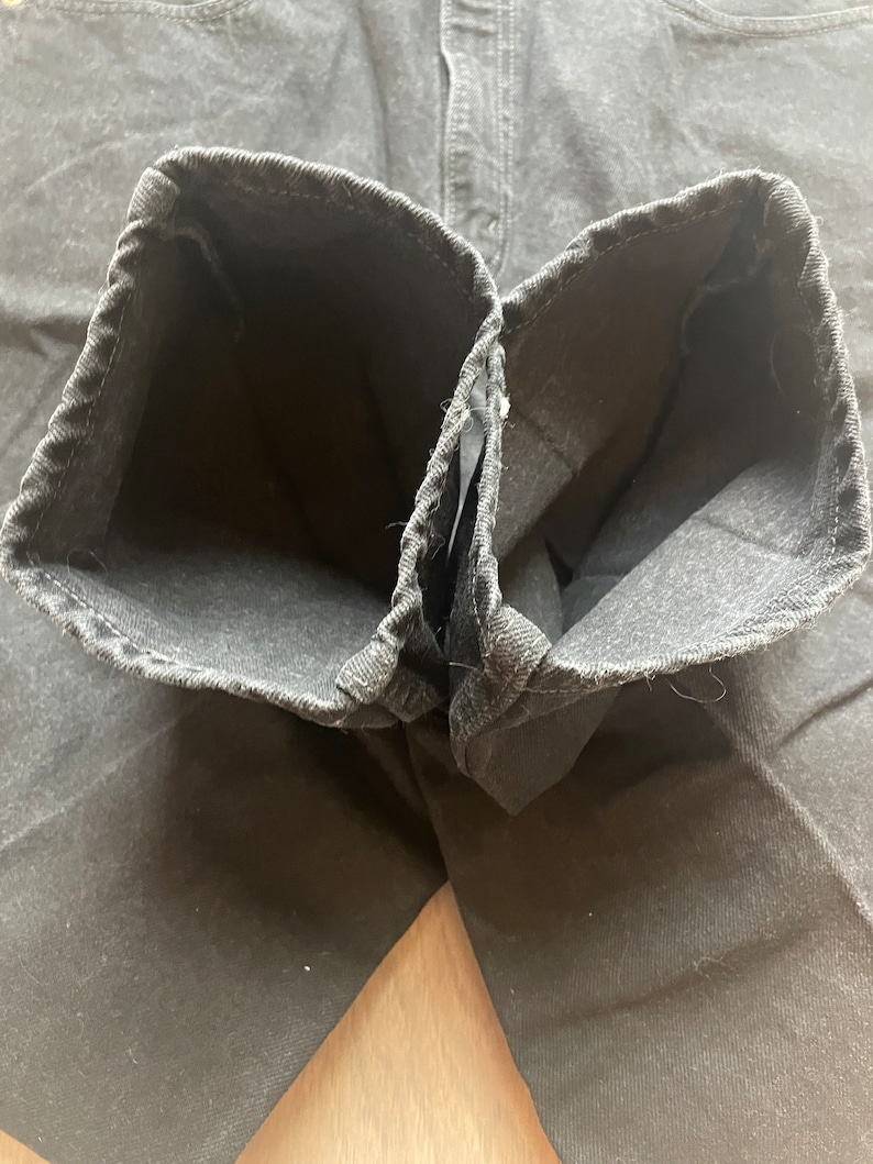 May include: Close-up of the inside of a pair of black denim jeans. The seams are visible and the fabric is soft and worn.