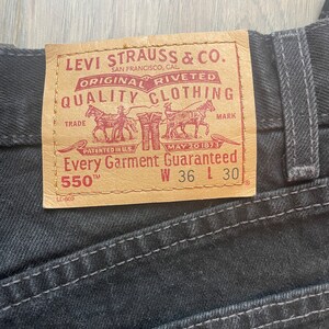 May include: A brown leather Levi Strauss & Co. patch with red text that reads "Original riveted quality clothing" and "Every garment guaranteed". The patch also includes a trade mark with a drawing of three horses pulling a wagon. The patch has the size information "W 36 L 30" and "550 TM".