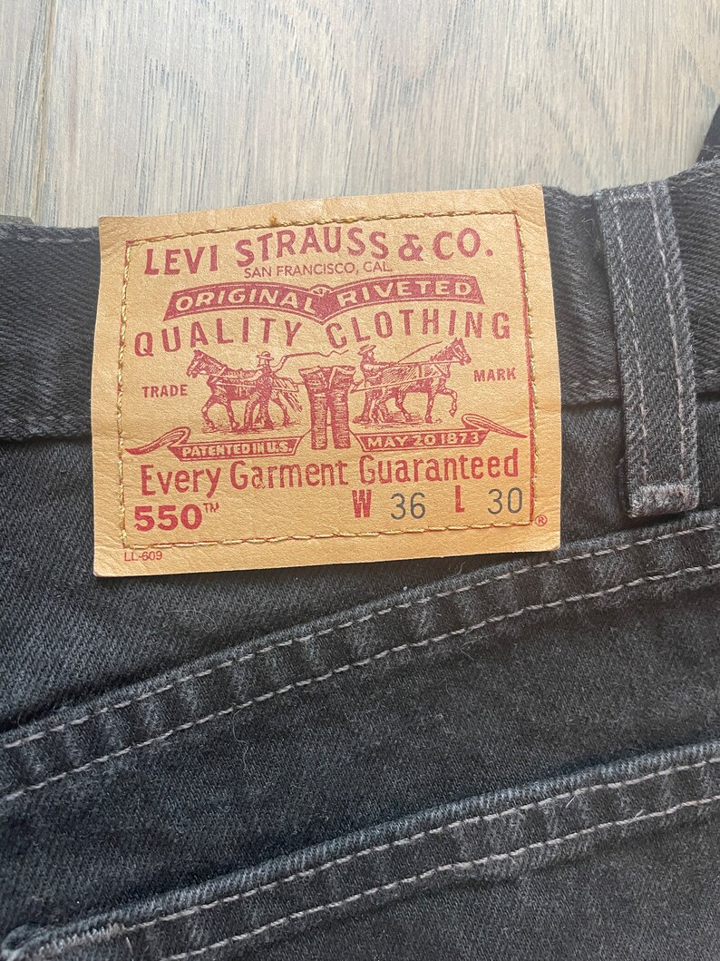 May include: A brown leather Levi Strauss & Co. patch with red text that reads "Original riveted quality clothing" and "Every garment guaranteed". The patch also includes a trade mark with a drawing of three horses pulling a wagon. The patch has the size information "W 36 L 30" and "550 TM".