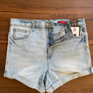 May include: Light blue denim shorts with a cuffed hem. The shorts have a zipper fly and a button closure. The label on the shorts reads "Curvy Rise The Denim Short 13x31".