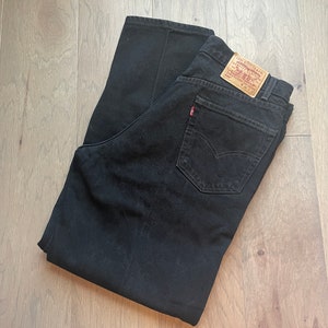 May include: A pair of black denim jeans with a Levi's label on the back pocket. The jeans are folded in half and laid flat on a wooden surface.