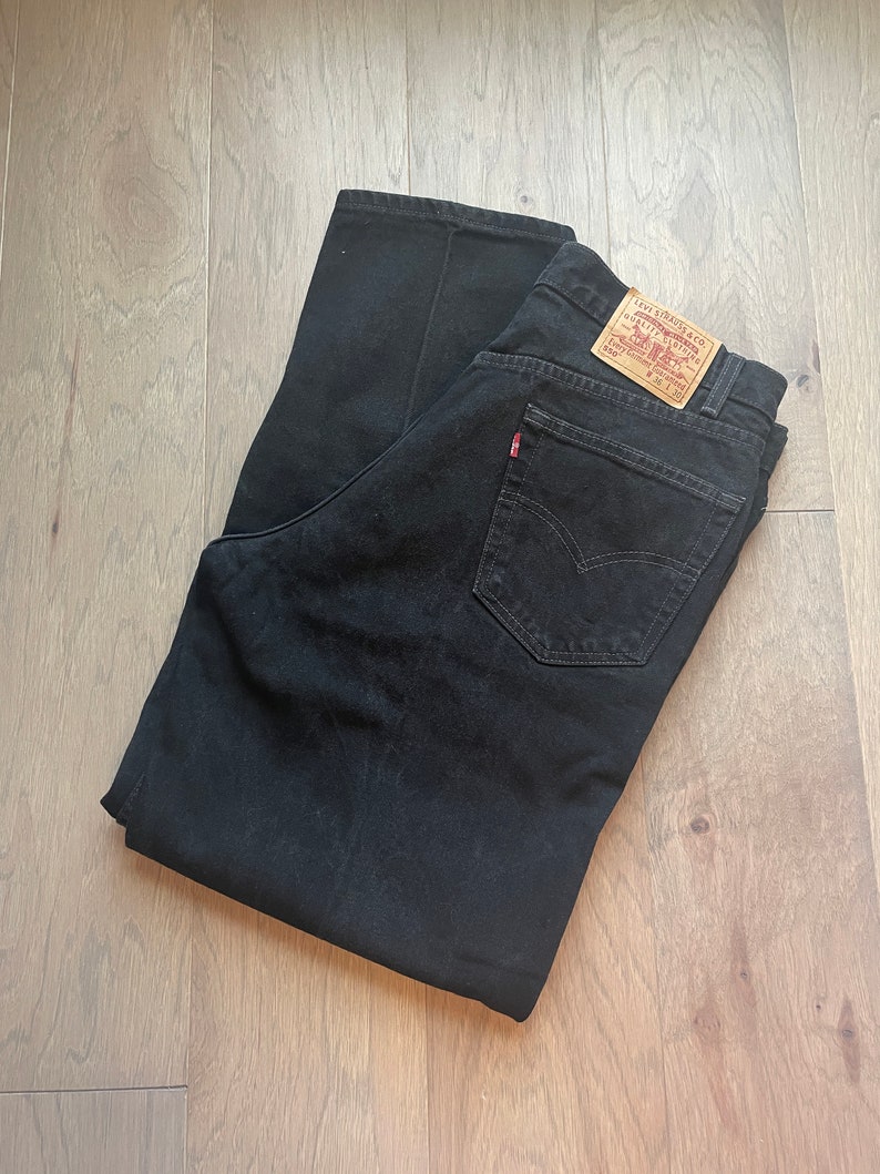 May include: A pair of black denim jeans with a Levi's label on the back pocket. The jeans are folded in half and laid flat on a wooden surface.