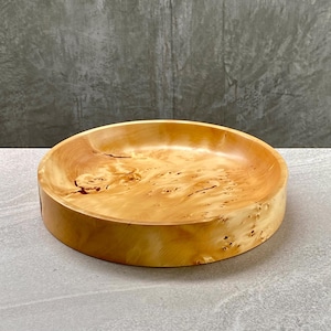 May include: A circular wooden bowl with a light-brown, natural finish. The bowl has a wide, shallow design and a smooth interior. The wood grain is visible, enhancing its rustic appeal. The bowl is likely for serving or display, with a diameter of approximately 25 cm.