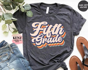 May include: A dark grey heather t-shirt with the text "Fifth Grade" in a retro rainbow design.