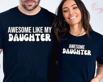 Puede incluir: Dos camisetas negras con texto blanco. La primera camiseta dice "Awesome Like My Daughter". La segunda camiseta dice "Awesome Daughter".