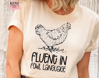 May include: A beige t-shirt with a black and white illustration of a chicken and the text "Fluent in Fowl Language".
