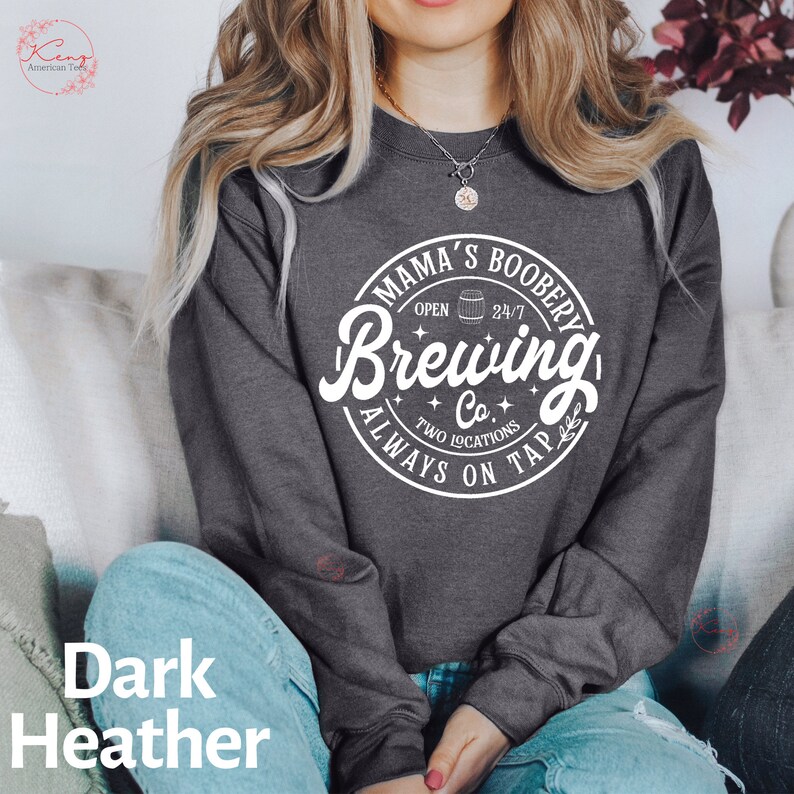 Puede incluir: Sudadera gris oscuro jaspeada con un estampado gr&aacute;fico blanco que dice "Mama's Boobery Brewing Co. Open 24/7 Two Locations Always On Tap" con un peque&ntilde;o icono de barril.