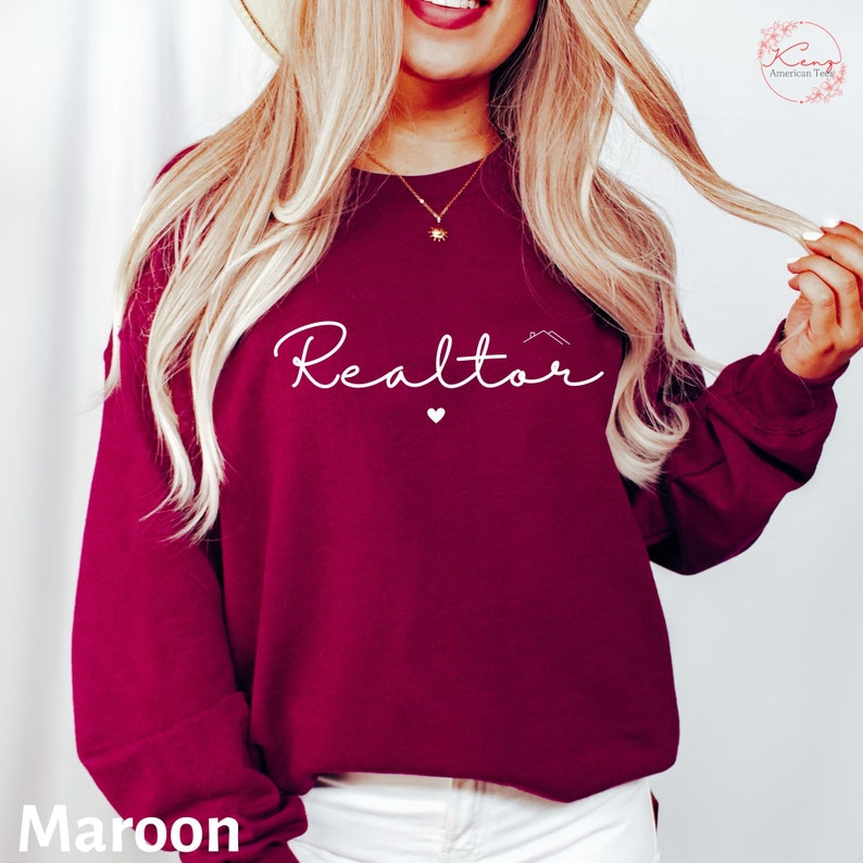 May include: Maroon sweatshirt with the word "Realtor" in white script with a small heart and house icon above the word.