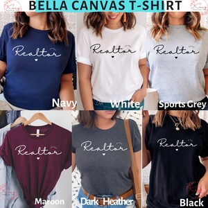 May include: A Bella Canvas t-shirt in six different colors: navy, white, sports grey, maroon, dark heather, and black. Each shirt features the word "Realtor" in white script with a small heart and a mountain graphic.