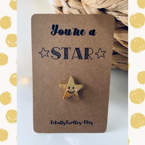 Könnte beinhalten: Eine goldene sternförmige Anstecknadel mit einem Smiley auf einer braunen Karte mit dem Text "You're a STAR" und "Totally Turtley-Etsy".