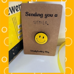 Op de afbeelding: Een bruine kaart met de tekst "Sending you a smile" en een gele smiley-speld. De kaart heeft ook de tekst "Totally Turtley-Etsy". De achtergrond is geel met witte cirkels.
