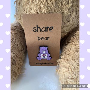 Peut inclure: Épingle en émail Share Bear violette sur une carte marron. L'épingle représente un ours souriant tenant un bouquet de fleurs. La carte porte les mots "share bear". Le nom de la boutique Etsy "Totally Turtle-Etsy" est imprimé en bas.