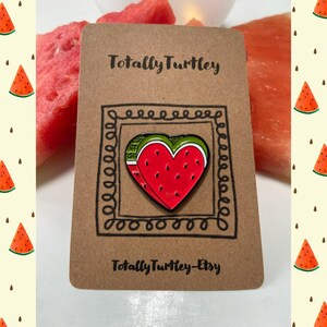 Puede incluir: Un pin de esmalte en forma de corazón que muestra una rodaja de sandía roja con semillas negras y corteza verde. El pin está sujeto a una tarjeta rectangular marrón con el texto Totally Turtley y Totally Turtley-Etsy impreso.