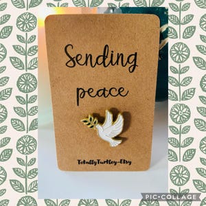 Op de afbeelding: Een bruine kaart met de woorden "Sending peace" in zwart schrift. Een witte duifspeld met een gouden olijftak is bevestigd. De Etsy shopnaam "TotallyTurtle-Etsy" staat onderaan afgedrukt.