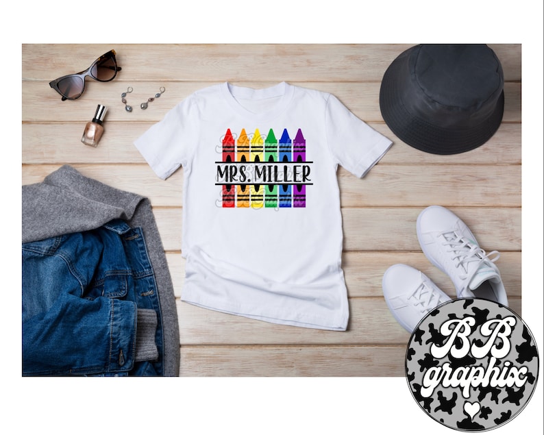 Pu&ograve; includere: Maglietta bianca con un design di matite colorate arcobaleno e il testo "MRS. MILLER" stampato su di essa.