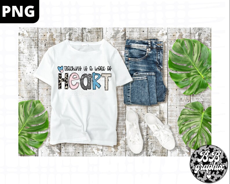 Op de afbeelding: Wit T-shirt met de tekst "Teaching is a work of heart" in kleurrijke letters met een luipaardprint. De letters zijn versierd met harten en andere patronen.